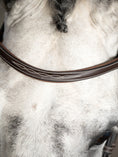 Load image into Gallery viewer, A classic hunter bridle with an English noseband and a solid throatlatch. The browband and noseband are beautifully decorated with a white décor stitching and are softly padded on the inside for increased comfort. The bridle is made in Spanish vegetable-tanned leather.
